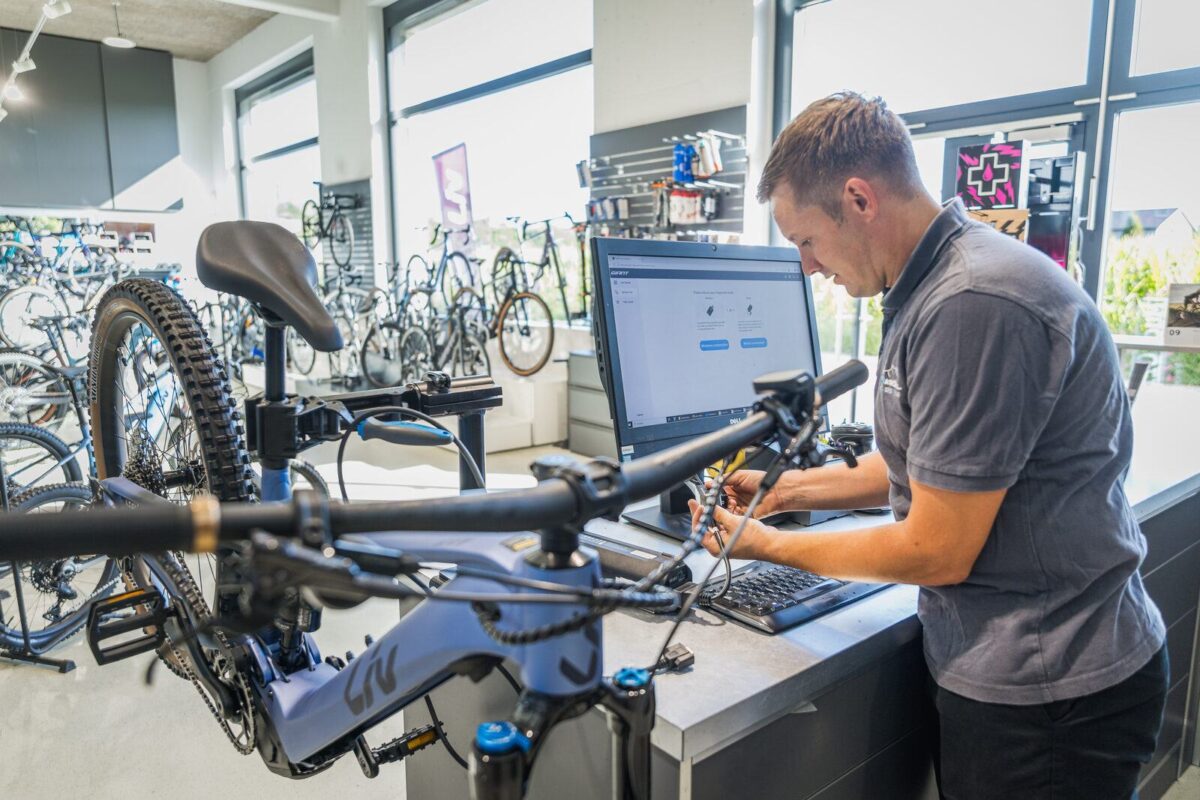 Mechaniker von Rad Kröll liest am Rechner den Fehlerspeicher eines E-Mountainbikes aus, das im Montageständer hängt