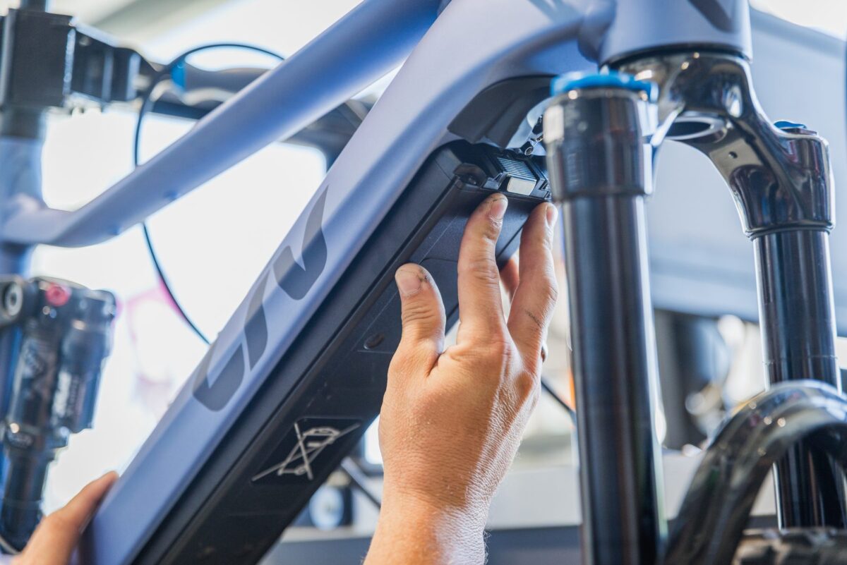 Hand am Dämpfer eines hellen Liv E-Mountainbikes, der Liv-Schriftzug am Rahmen ist im Bild